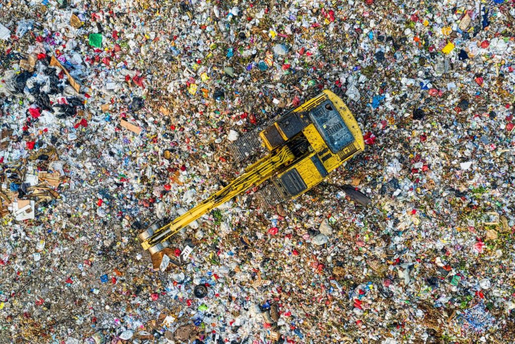 Birds eye view of an excavator digging through a trash in a garbage dump